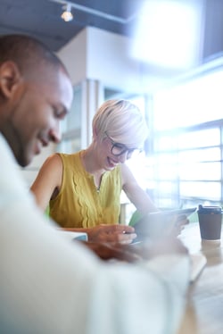 Two creative millenial small business owners working on social media strategy using a digital tablet while sitting at desk